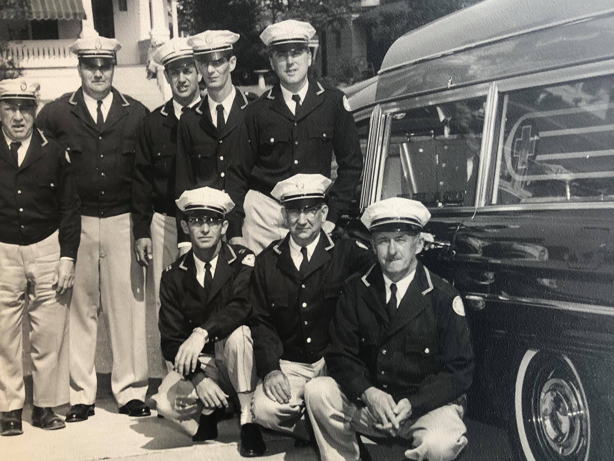 Group of men in formal uniforms in front of the ambulance